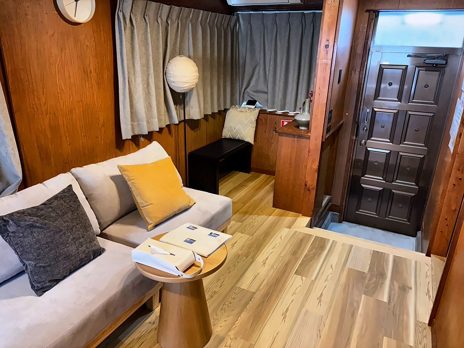 A compact living space with a sofa, a small table, a lamp, and a door leading to an outdoor area.