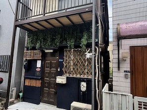 Un edificio residencial con fachada azul oscuro, una puerta marrón y una valla de madera con celosías.