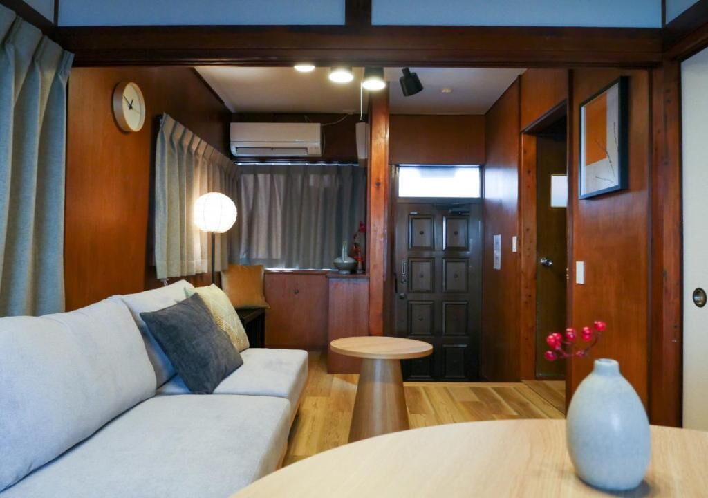 A room with a sofa, a table, a vase, a clock, and a door.