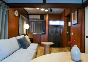 A room with a sofa, a table, a vase, a clock, and a door. - MSTAY Oshiage One (Sumida-ku)