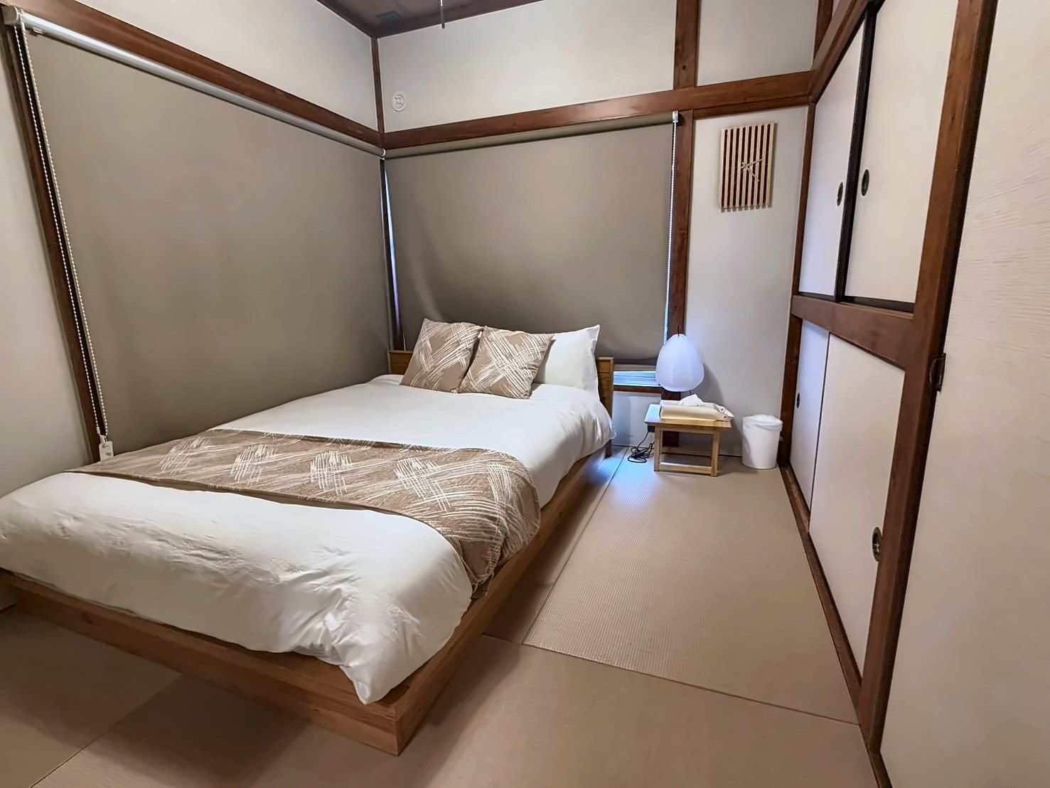 A bedroom with a bed, bedside table, lamp, and a small trash bin.