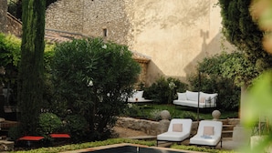 A pool area with lounge chairs, a stone wall, and greenery. - Luxury 6BR House in Eygalières Provence - Hotel Services, Pool, Sauna (Eygalières)