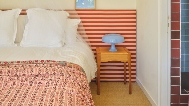 A bedroom with a bed, a bedside table with a lamp, a framed picture on the wall, and a door leading to a tiled area. - Luxury 6BR House in Eygalières Provence - Hotel Services, Pool, Sauna (Eygalières)
