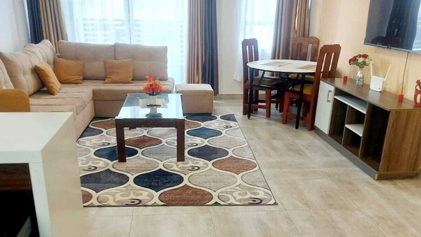 A living room with a sofa, coffee table, and dining area with chairs and a table. - The Enkang View Palace Apartment (Nairobi)