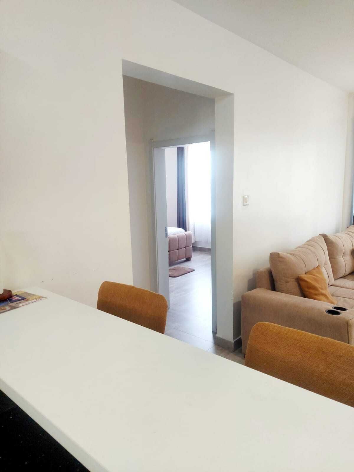A modern living room with a sofa, a dining table with chairs, and a doorway leading to another room.