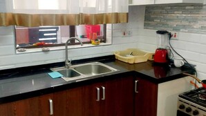 A kitchen with a sink, a stove, and a window with curtains. - The Enkang View Palace Apartment (Nairobi)