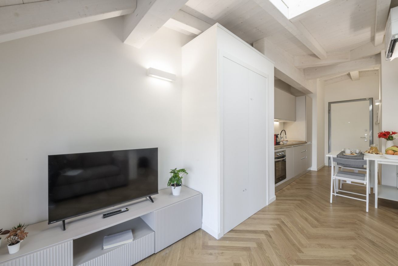 Una sala de estar moderna con un televisor de pantalla plana, una planta pequeña y un mueble blanco para entretenimiento.