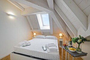 A bedroom with a skylight, a bed with white linens, a bedside table with a vase and wine glasses, and a small table with a bowl and a bottle. - NOVARA, 62 – Sky Loft Milan (Milano)