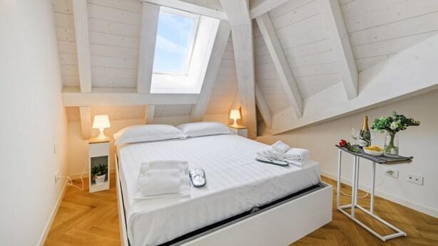 A bedroom with a skylight, a bed, bedside tables, and a small table with a vase and flowers. - NOVARA, 62 – Sky Loft Milan (Milano)