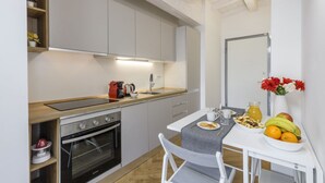 A compact kitchen with a built-in oven, a small dining table with chairs, and a fruit bowl on the counter. - NOVARA, 62 – Sky Loft Milan (Milano)