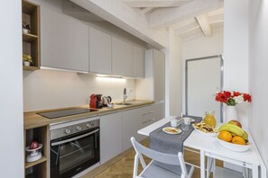 A compact kitchen with a built-in oven, a small dining table with chairs, and a fruit bowl on the counter. - NOVARA, 62 – Sky Loft Milan (Milano)