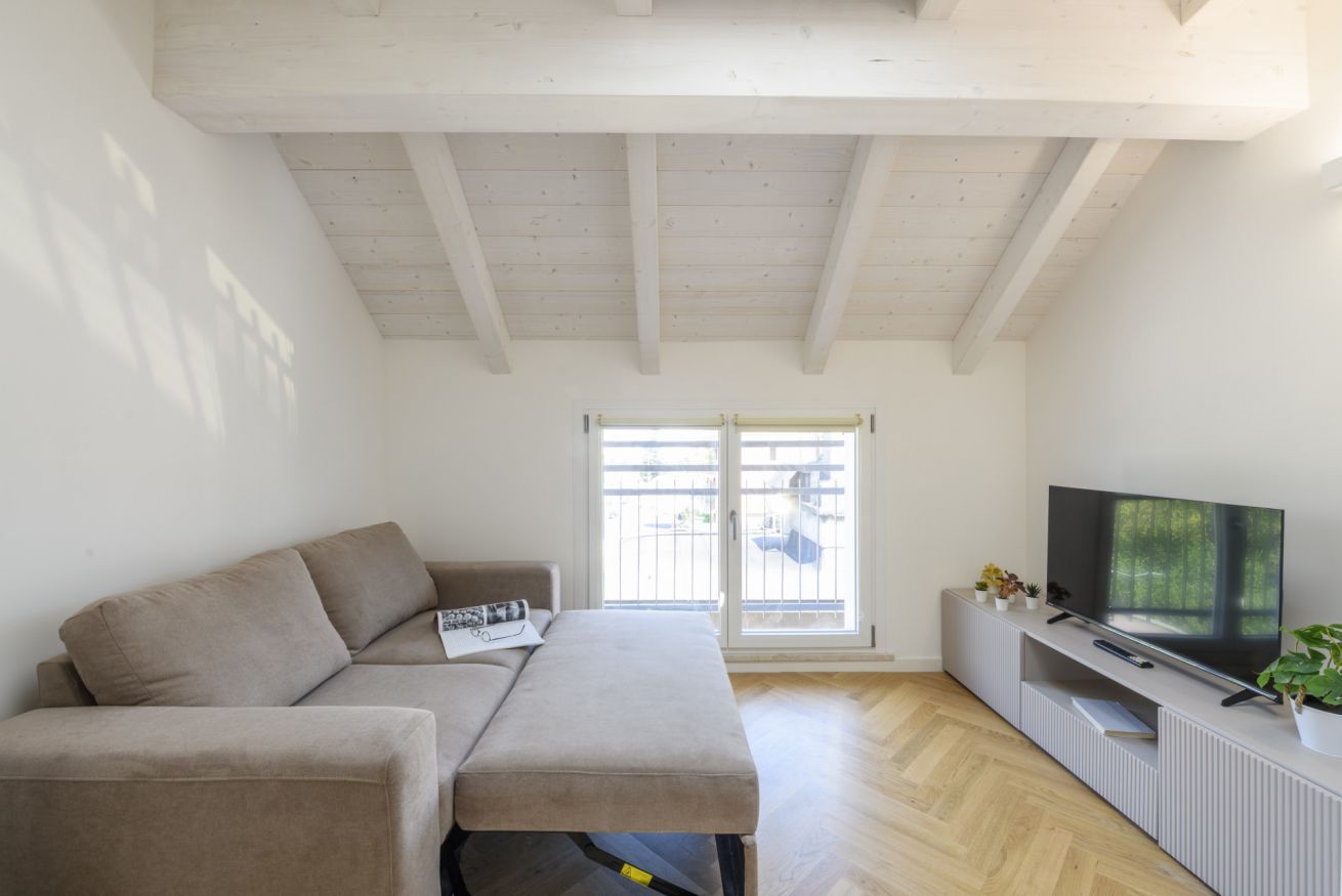 A living room with a sofa, a television, and a window with blinds.