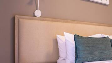 Quarto de hotel com uma cama, mesa de cabeceira com telefone, luminária na parede e um quadro.
