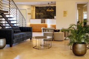 Zona de recepción de un hotel con mostrador, escalera y asientos.