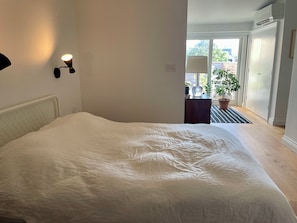 A bedroom with a bed, a nightstand, a lamp, and a view of the outdoors through a door. - Designer Light Filled 2BR House in Kensington w/Rooftop patio (Toronto)