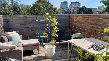 An outdoor patio with a wooden deck, a cushioned seating area, a table with chairs, and potted plants.