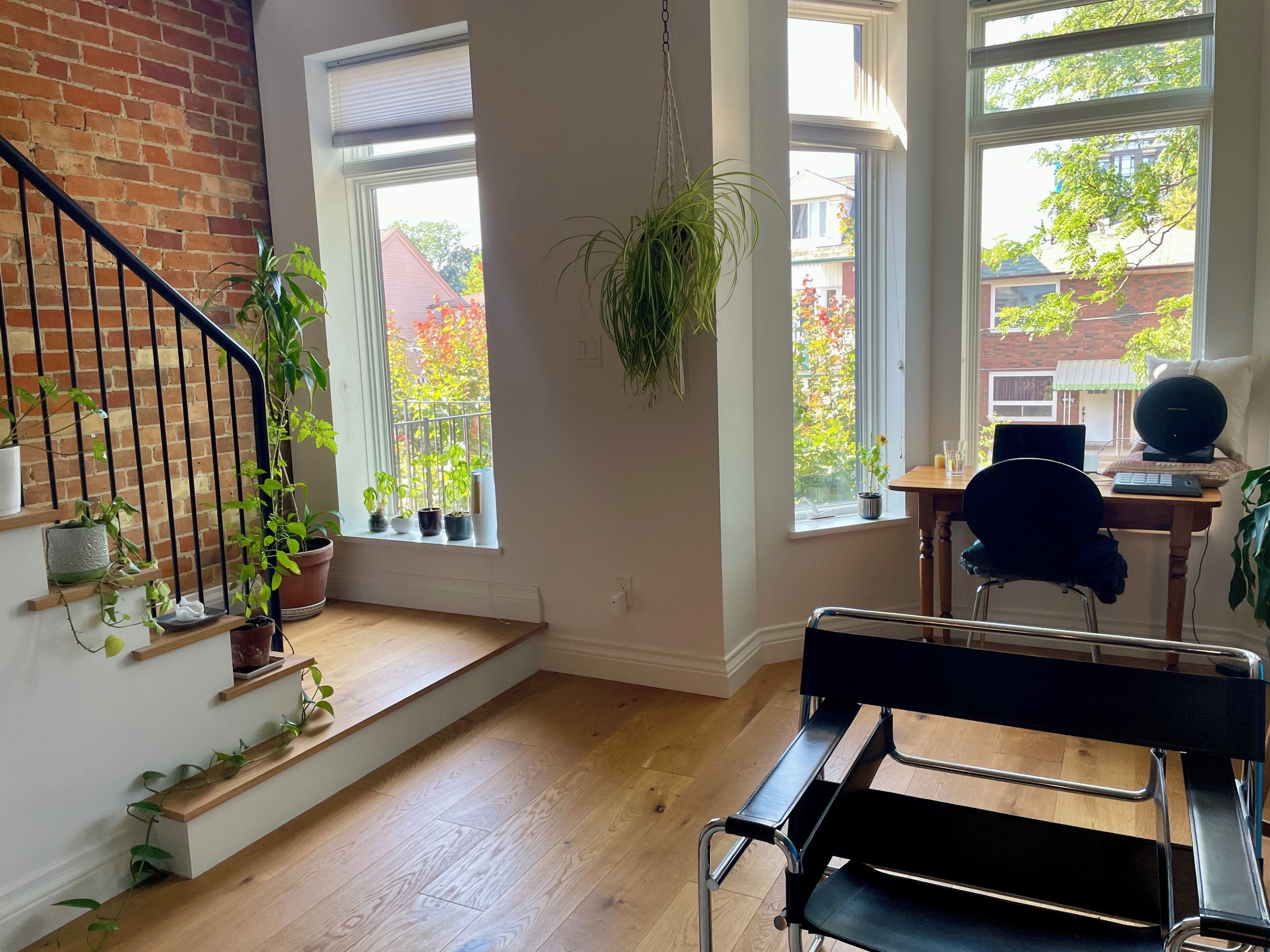 A room with a staircase, a desk with a computer, and multiple potted plants.
