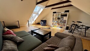 Um quarto no estilo loft, com teto inclinado, sofá, mesa de centro, estante e bateria.