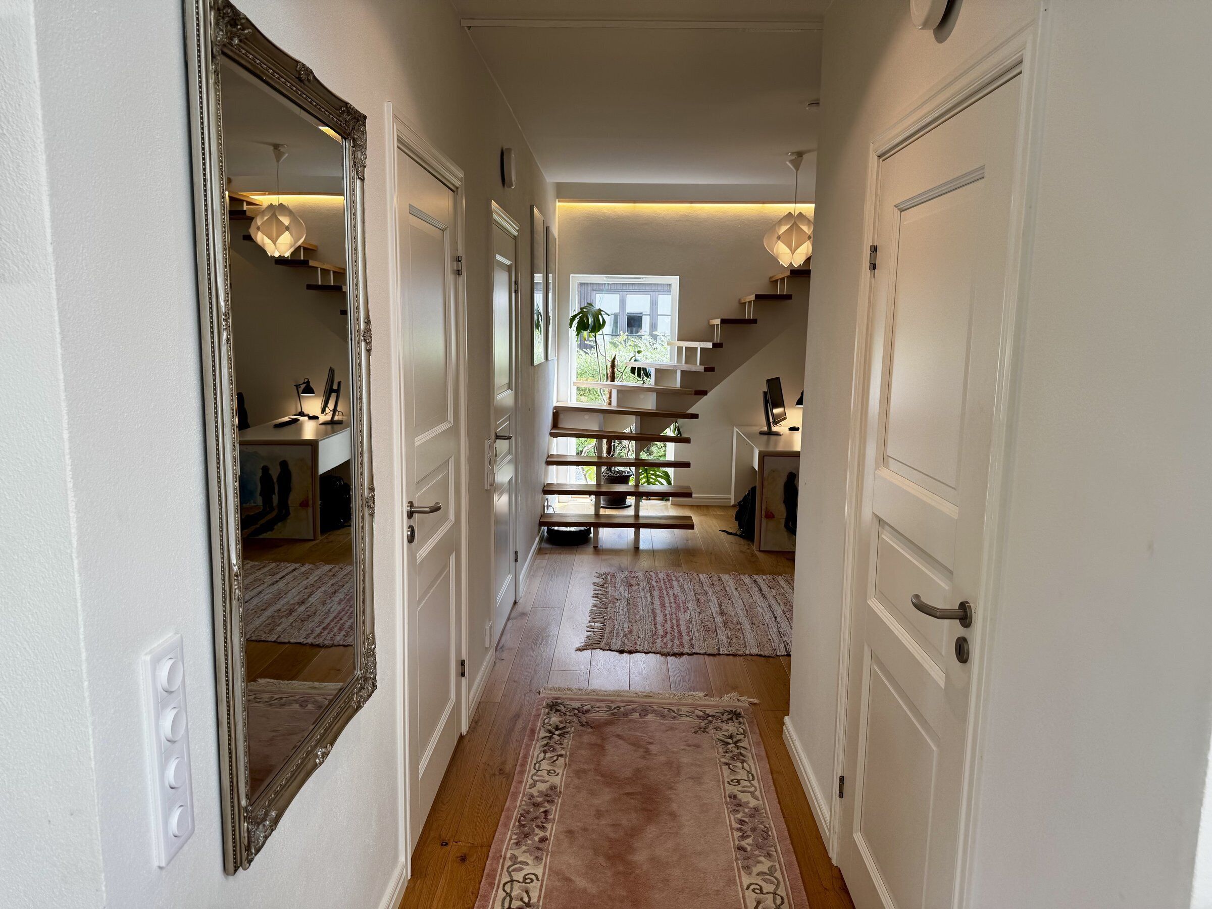 A hallway with a staircase leading to a second floor, a large mirror, and a rug.