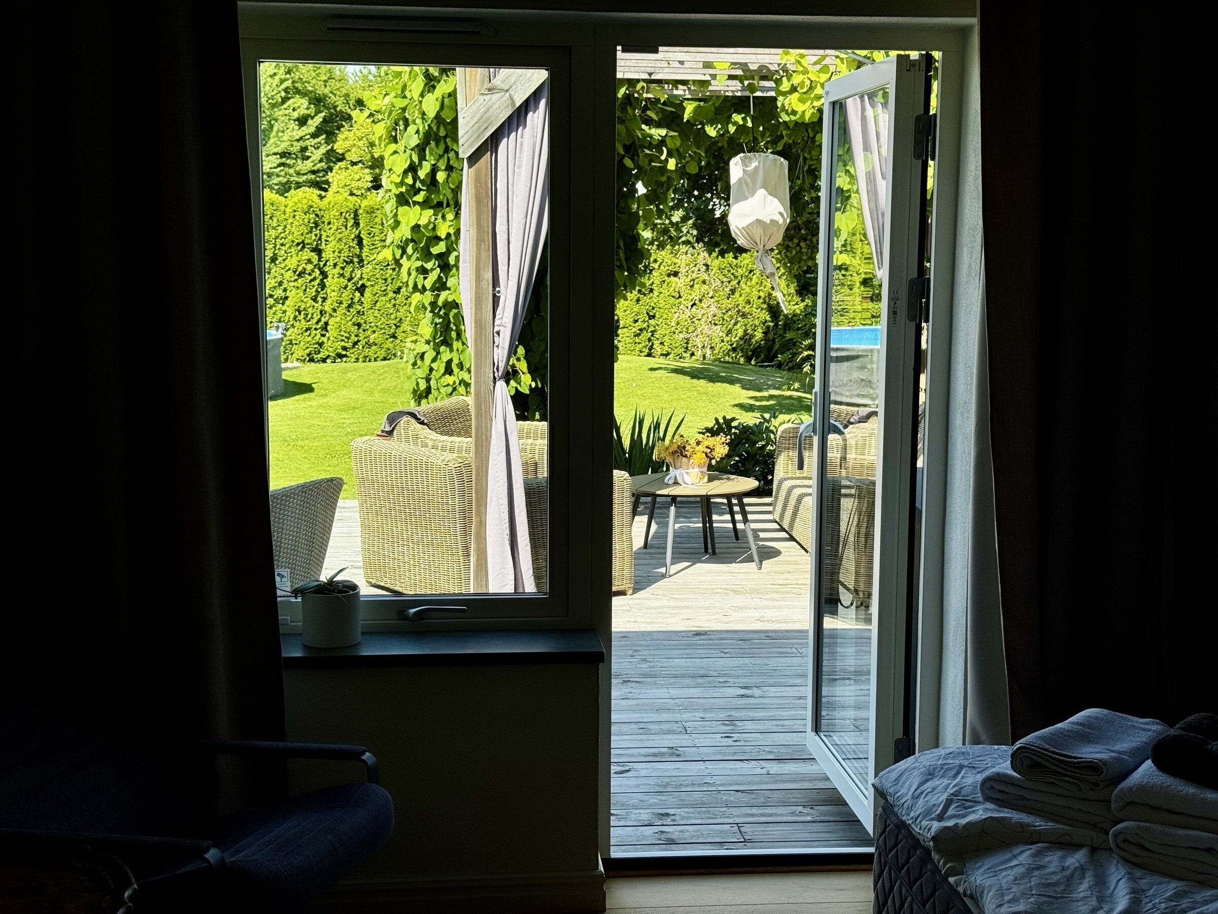 Ein Zimmer mit einer Schiebetür, die auf eine Terrasse mit Korbmöbeln und einem kleinen Tisch mit Blumen führt.