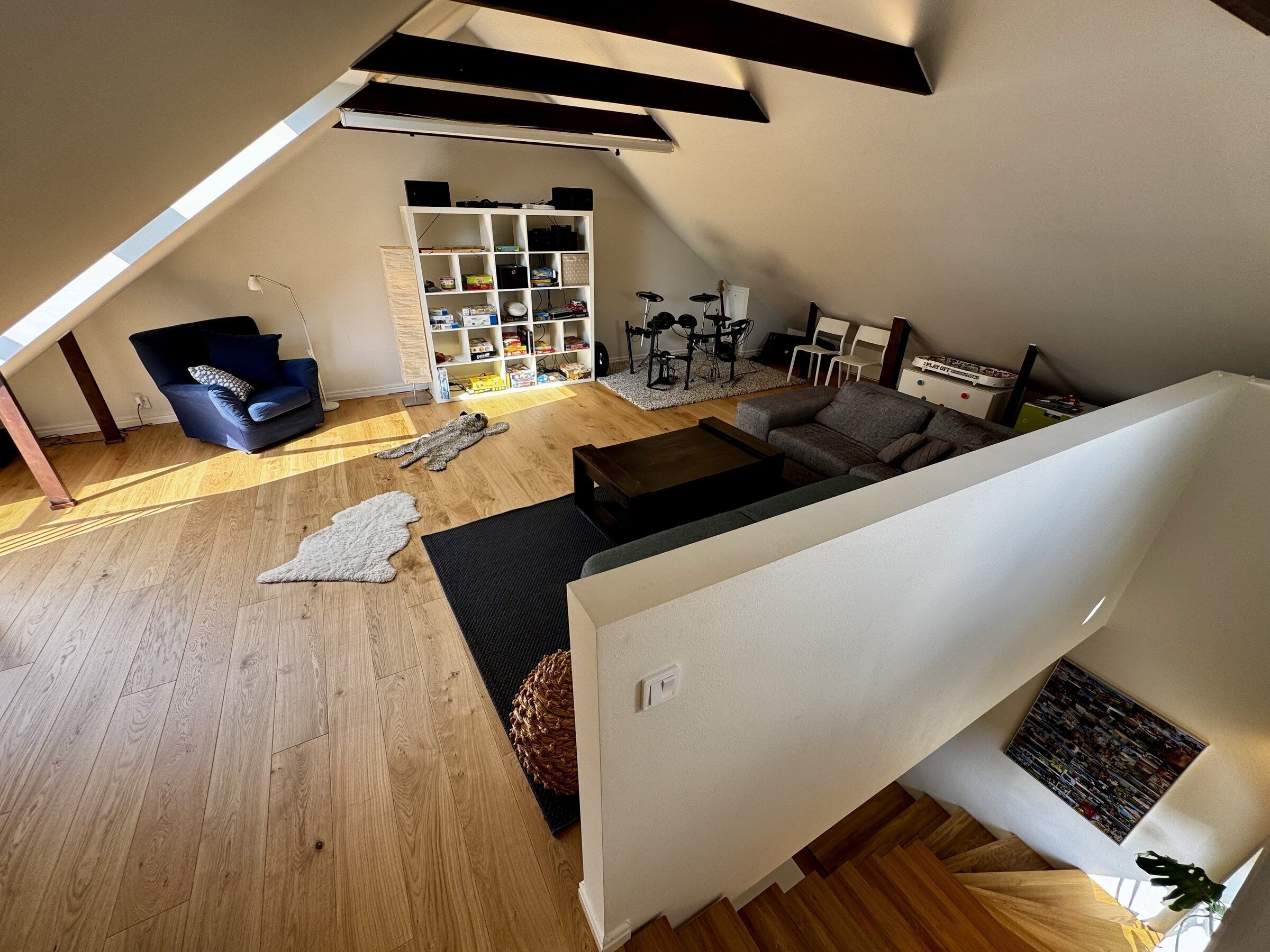 Un espacio habitable tipo loft con techo inclinado, estantería empotrada, batería y sofá.