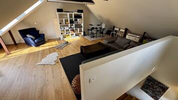 Un espacio habitable tipo loft con techo inclinado, estantería empotrada, batería y sofá.