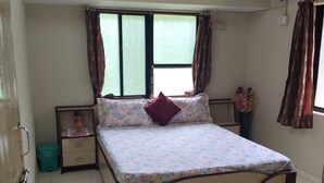 A bedroom with a bed, a nightstand, a window with curtains, a ceiling fan, and a wall-mounted light fixture.