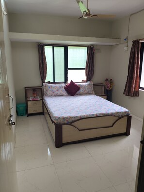 A bedroom with a bed, a nightstand, a window with curtains, a ceiling fan, and a wall-mounted light fixture.