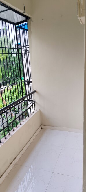 A corner of a room with a balcony, white walls, and a tiled floor.