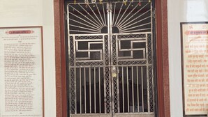 A temple entrance with a large ornate door, a religious painting above, and informational plaques on either side.