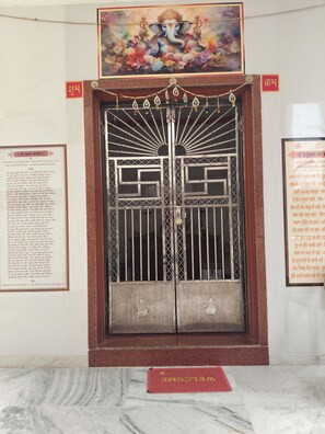 A temple entrance with a large ornate door, a religious painting above, and informational plaques on either side.