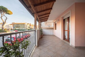 A balcony with a tiled floor, a wooden ceiling, and a view of parked cars and buildings.