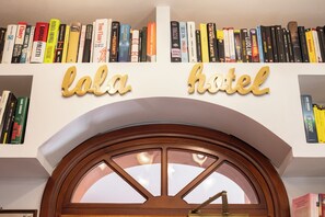Entrada de un hotel con un arco de madera y una estantería superior con varios libros.