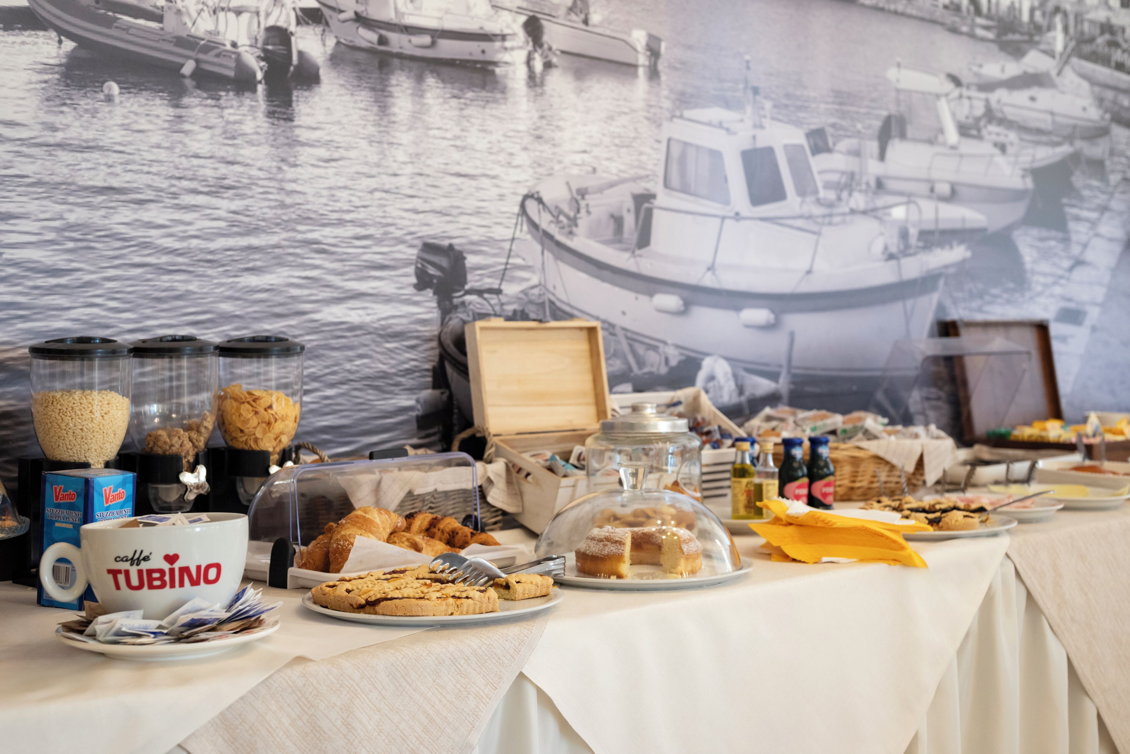A buffet table with various food items, a coffee station, and a backdrop of a boat on water.