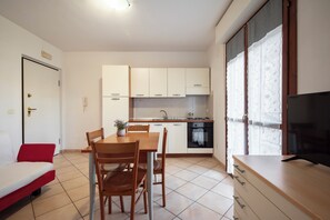 Un espacio habitable compacto con kitchenette, un comedor con mesa y sillas, un sofá y una televisión.