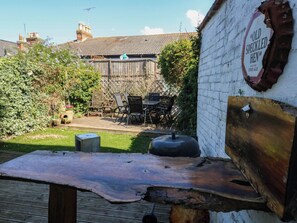 A rustic outdoor seating area with a wooden table and chairs, a brick wall with a sign, and a garden with a fence and greenery. - Driftmark (Weymouth)