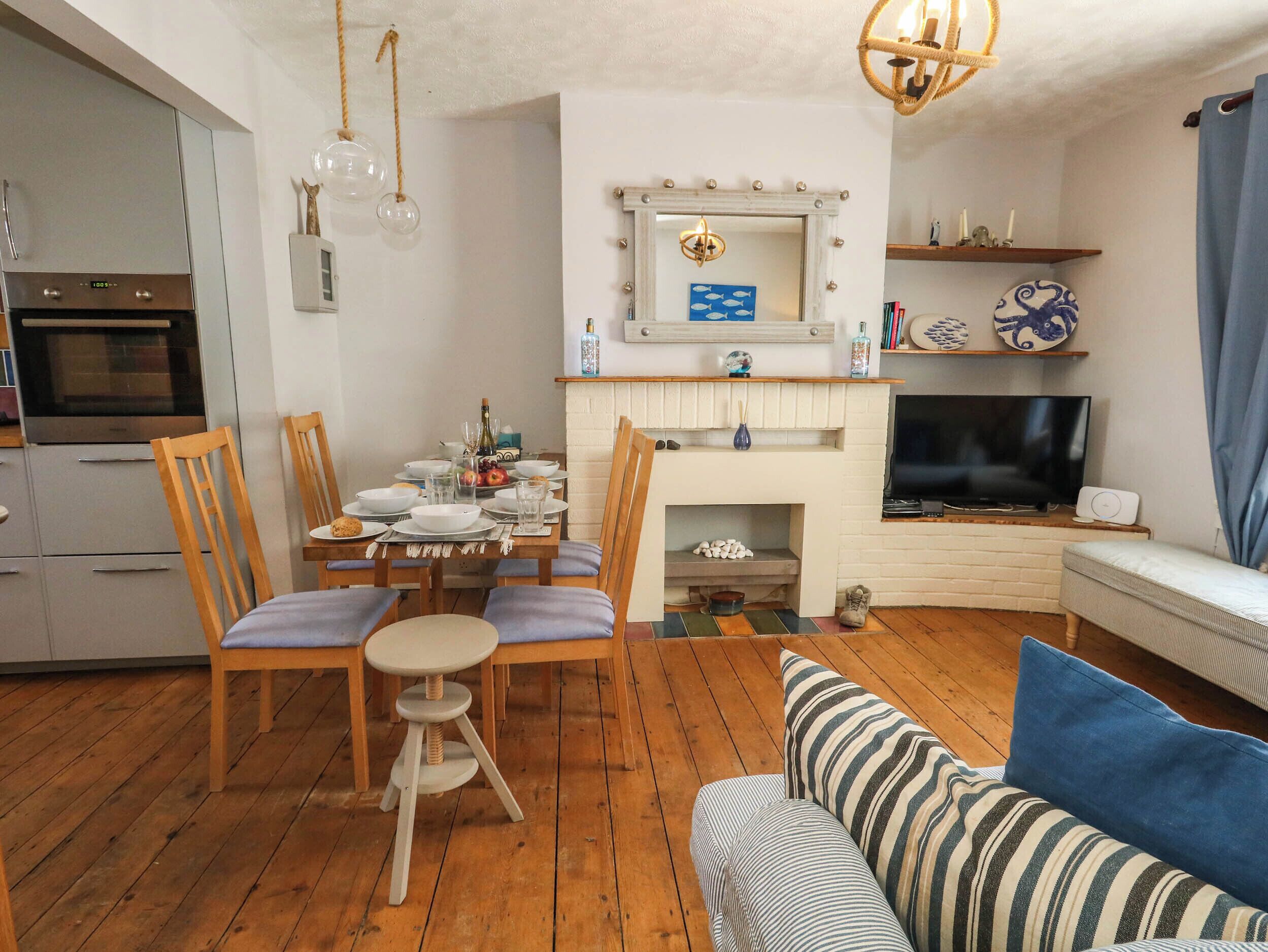 A modern living room with a dining area, wooden flooring, a fireplace, a television, and a kitchen with a built-in oven.