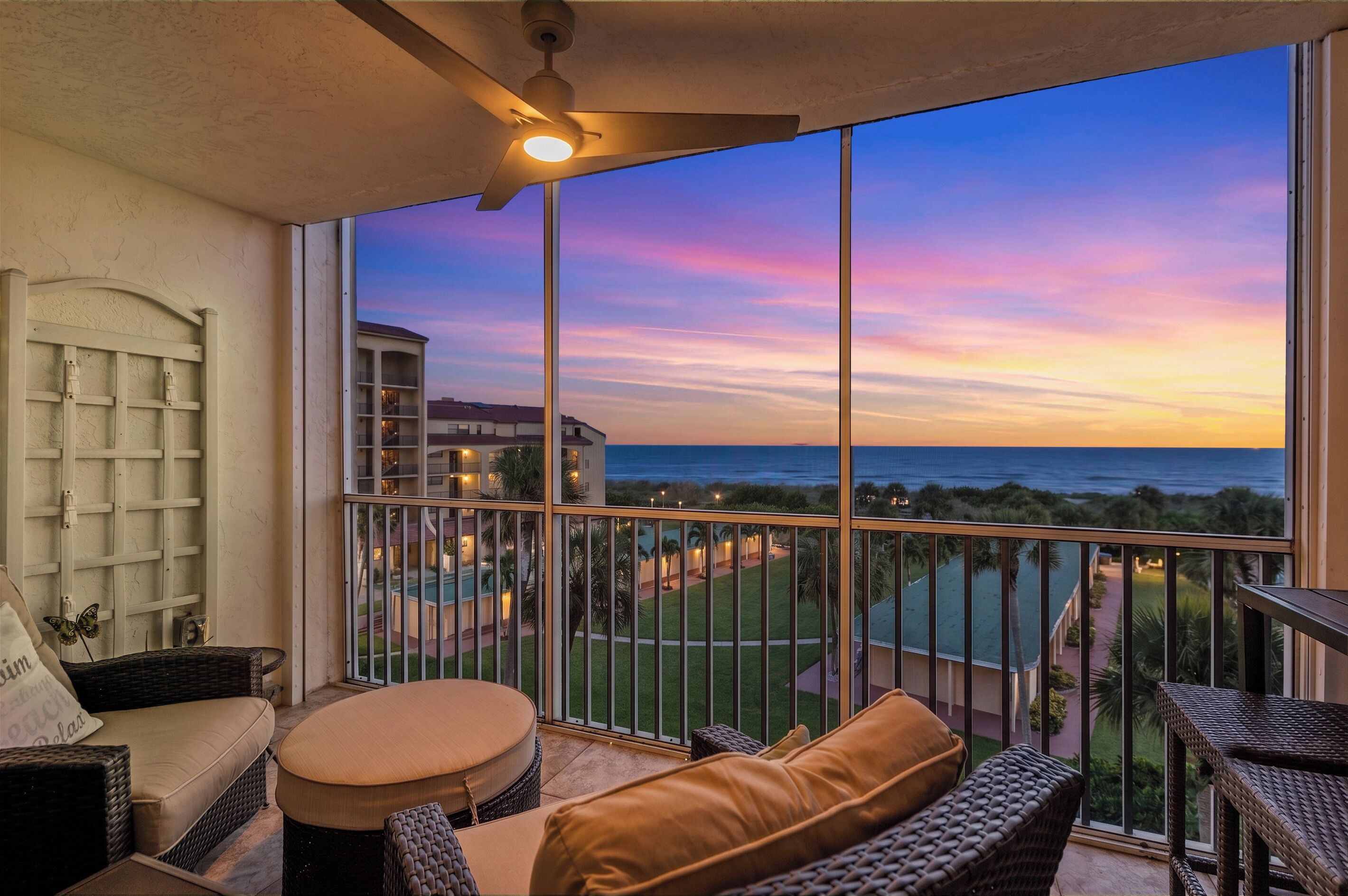 Een balkon met uitzicht op een resort en de oceaan bij zonsondergang.