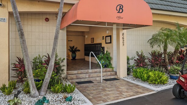 A hotel entrance with a covered awning, a staircase, and a parking area with a red vehicle. - Between Blues | SK Collection by Siesta Stays (Sarasota)