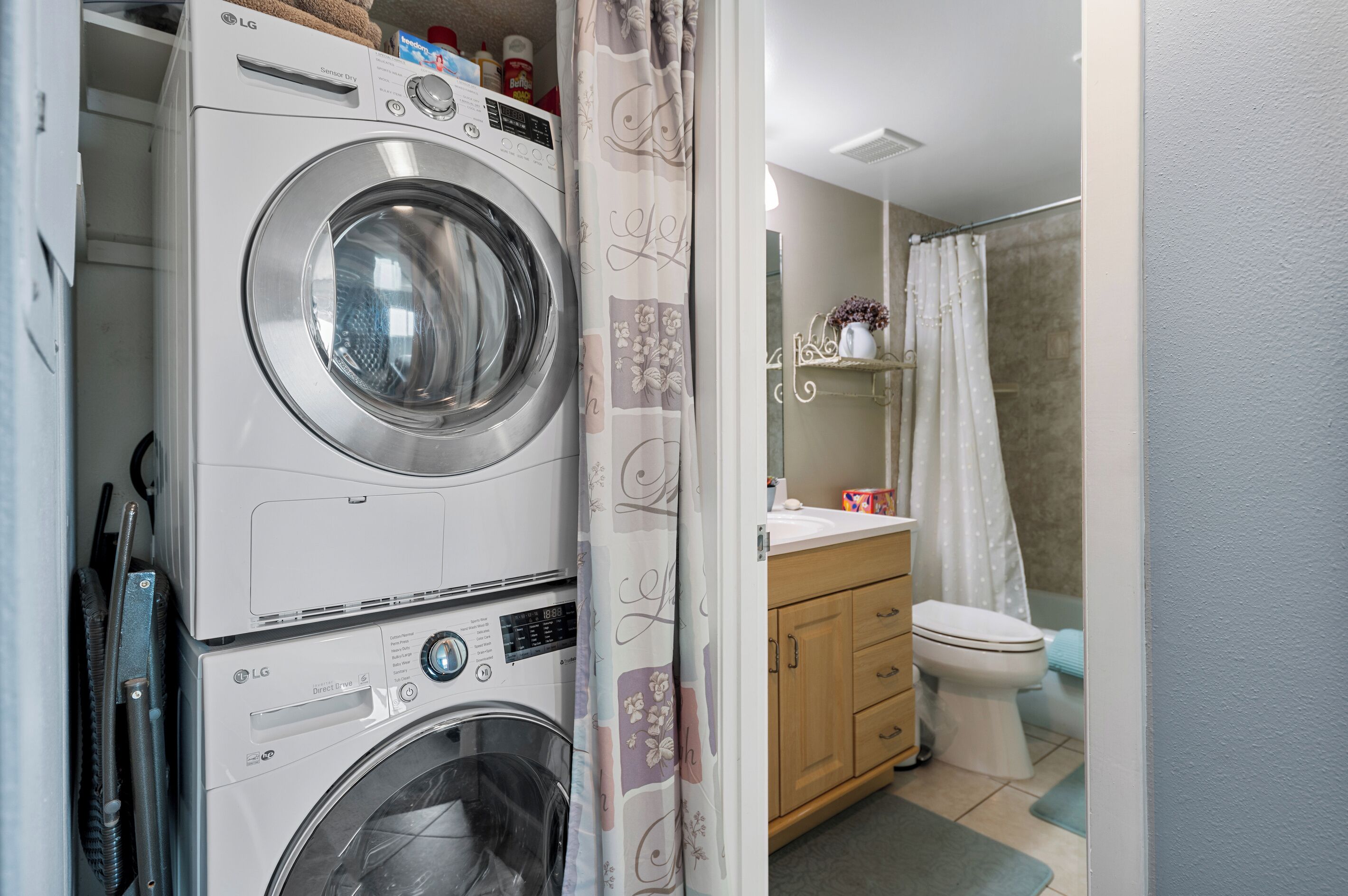 Un espace buanderie compact comprenant un lave-linge et un sèche-linge à chargement frontal, un meuble en bois et une douche avec un rideau.