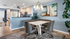 A modern kitchen with a dining area, featuring a chandelier, a painting of a beach scene, and a large potted plant. - Between Blues | SK Collection by Siesta Stays (Sarasota)