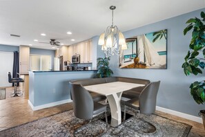 A modern kitchen with a dining area, featuring a chandelier, a painting of a beach scene, and a large potted plant. - Between Blues | SK Collection by Siesta Stays (Sarasota)