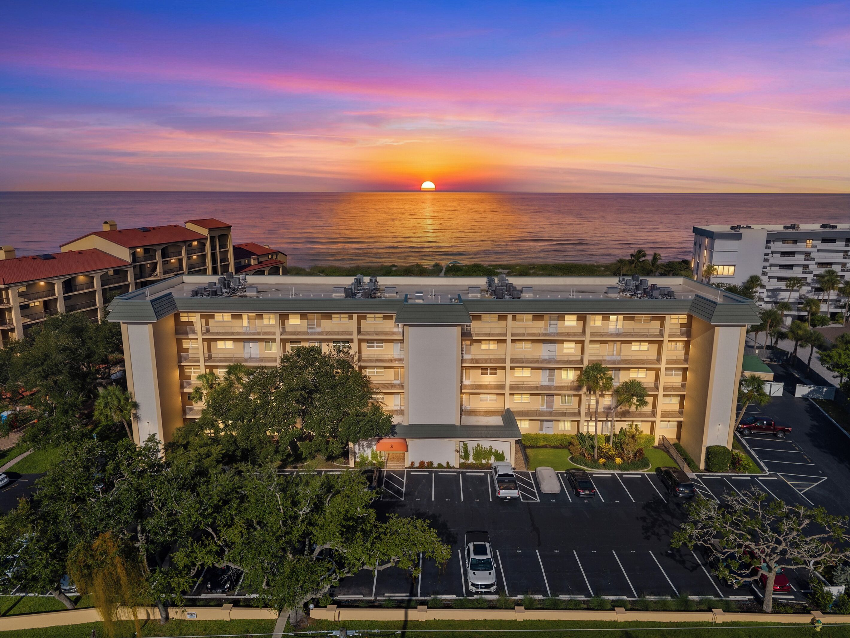 Un hotel de varios pisos con estacionamiento y vista al océano al atardecer.