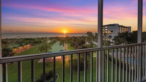 A sunset view from a balcony overlooking a golf course and a building with multiple floors. - Between Blues | SK Collection by Siesta Stays (Sarasota)