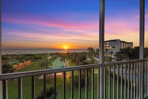 A sunset view from a balcony overlooking a golf course and a building with multiple floors. - Between Blues | SK Collection by Siesta Stays (Sarasota)