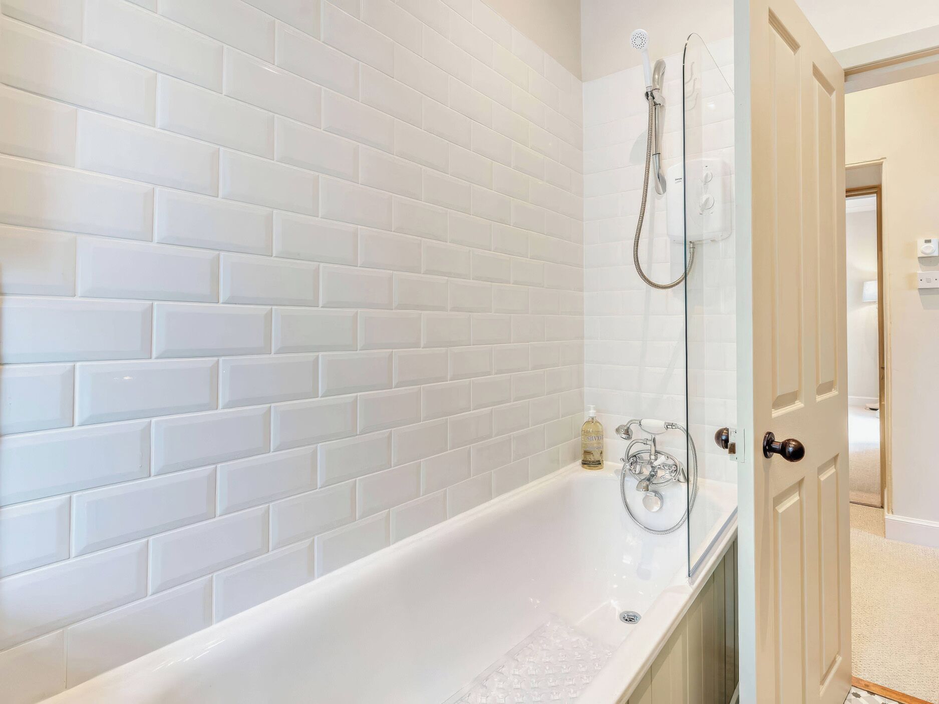 A bathroom with white tiled walls, a bathtub, and a shower.