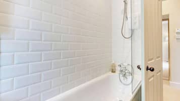 A bathroom with white tiled walls, a bathtub, and a shower.