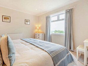 A bedroom with a bed, a bedside table with a lamp, a window with curtains, and a radiator.