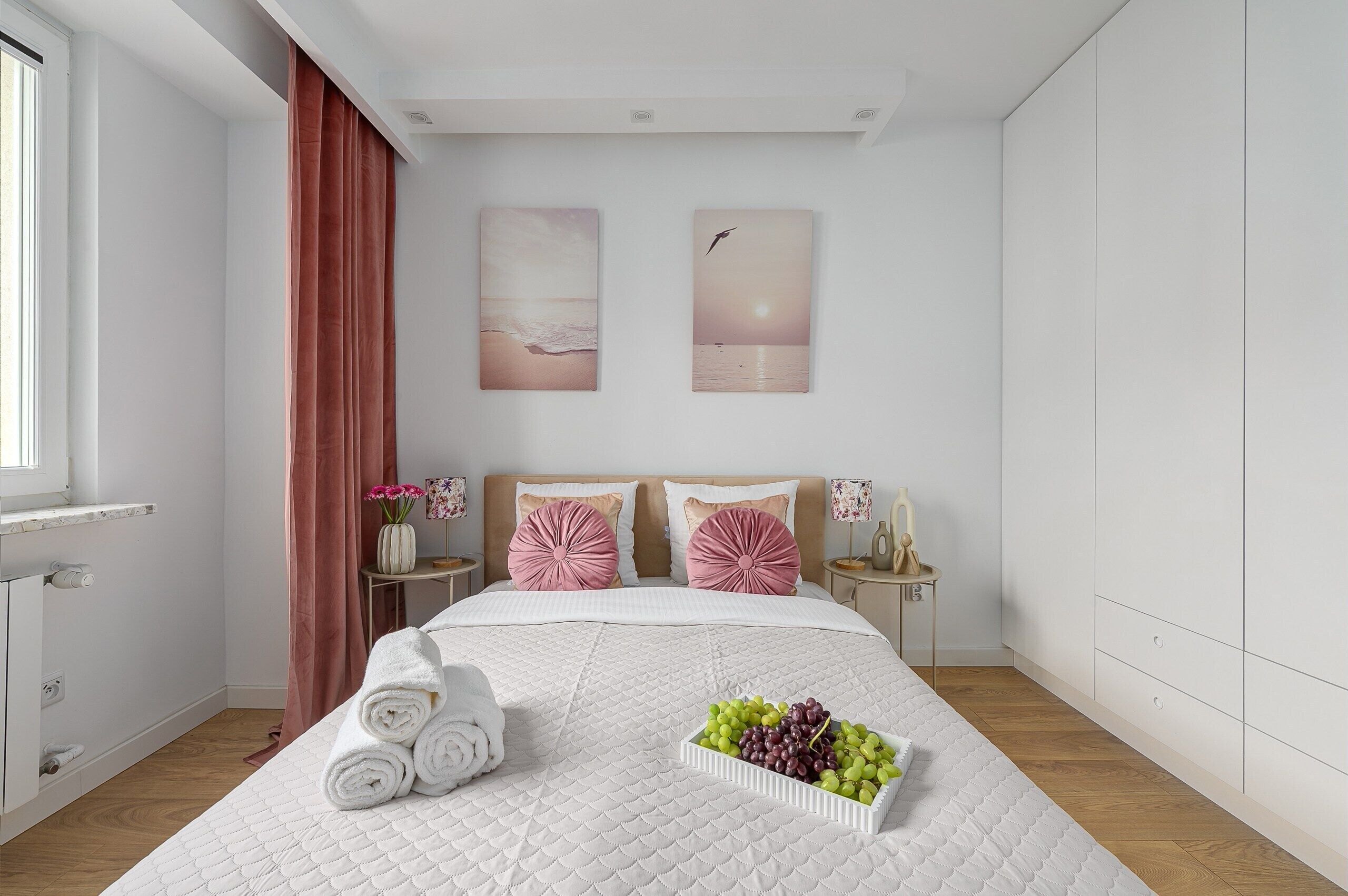 A modern bedroom with a bed, a bedside table, a nightstand, a window, and a wall with two paintings.