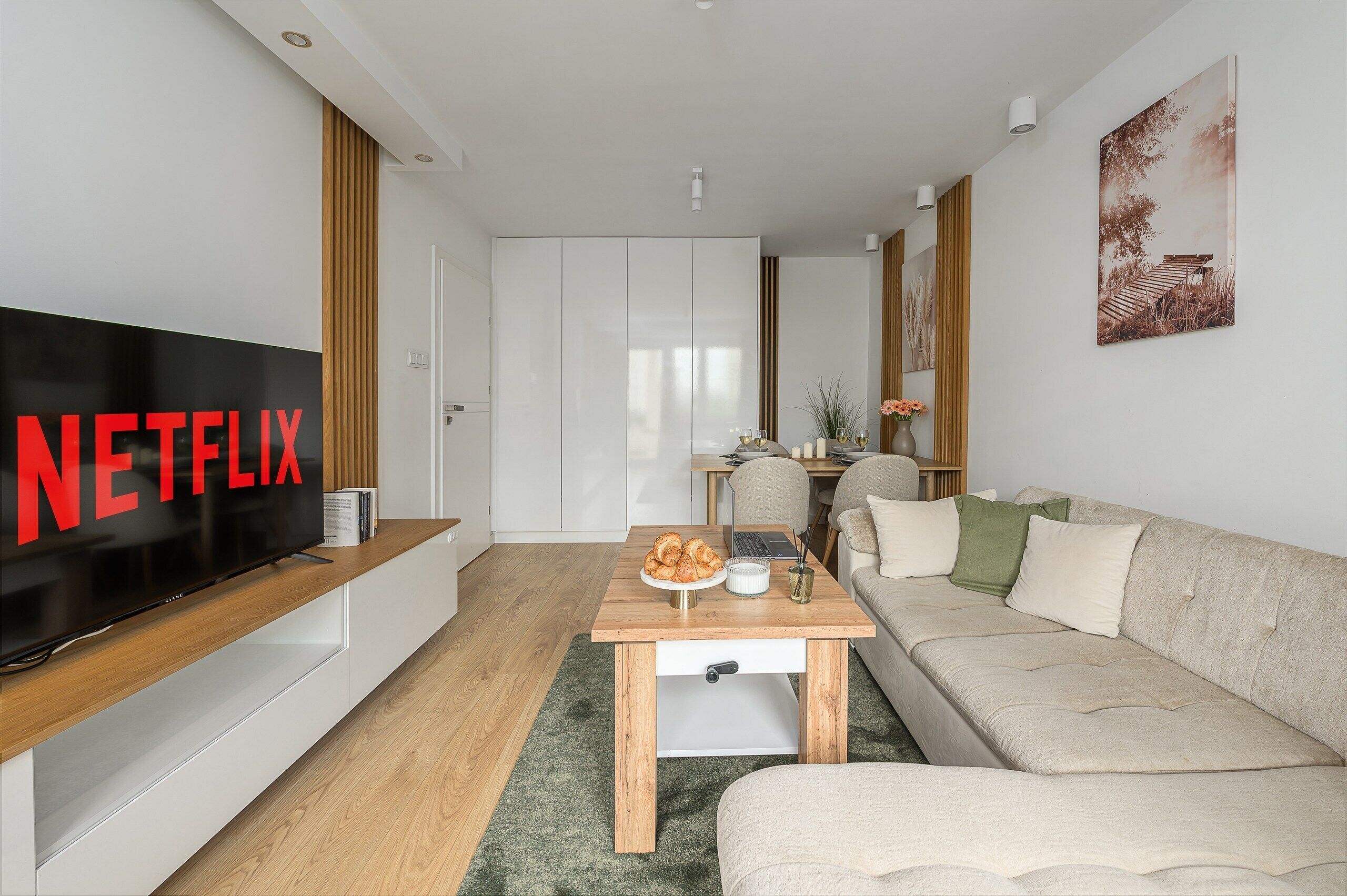Moderni olohuone, jossa on litteänäyttöinen televisio, puuhuonekalut, sohva ja ruokailutila, jossa on pöytä kahdelle.